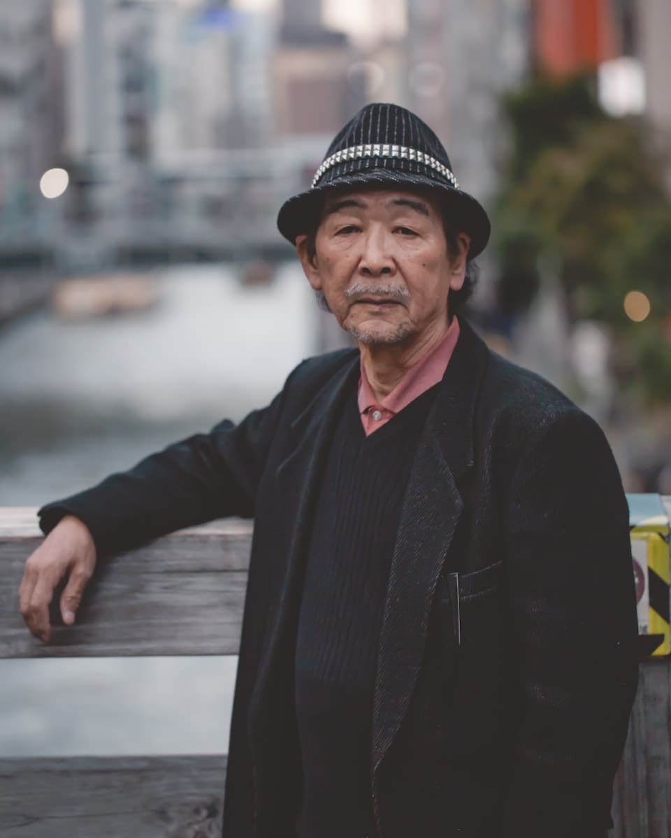 man wearing black hat standing against wooden handrail